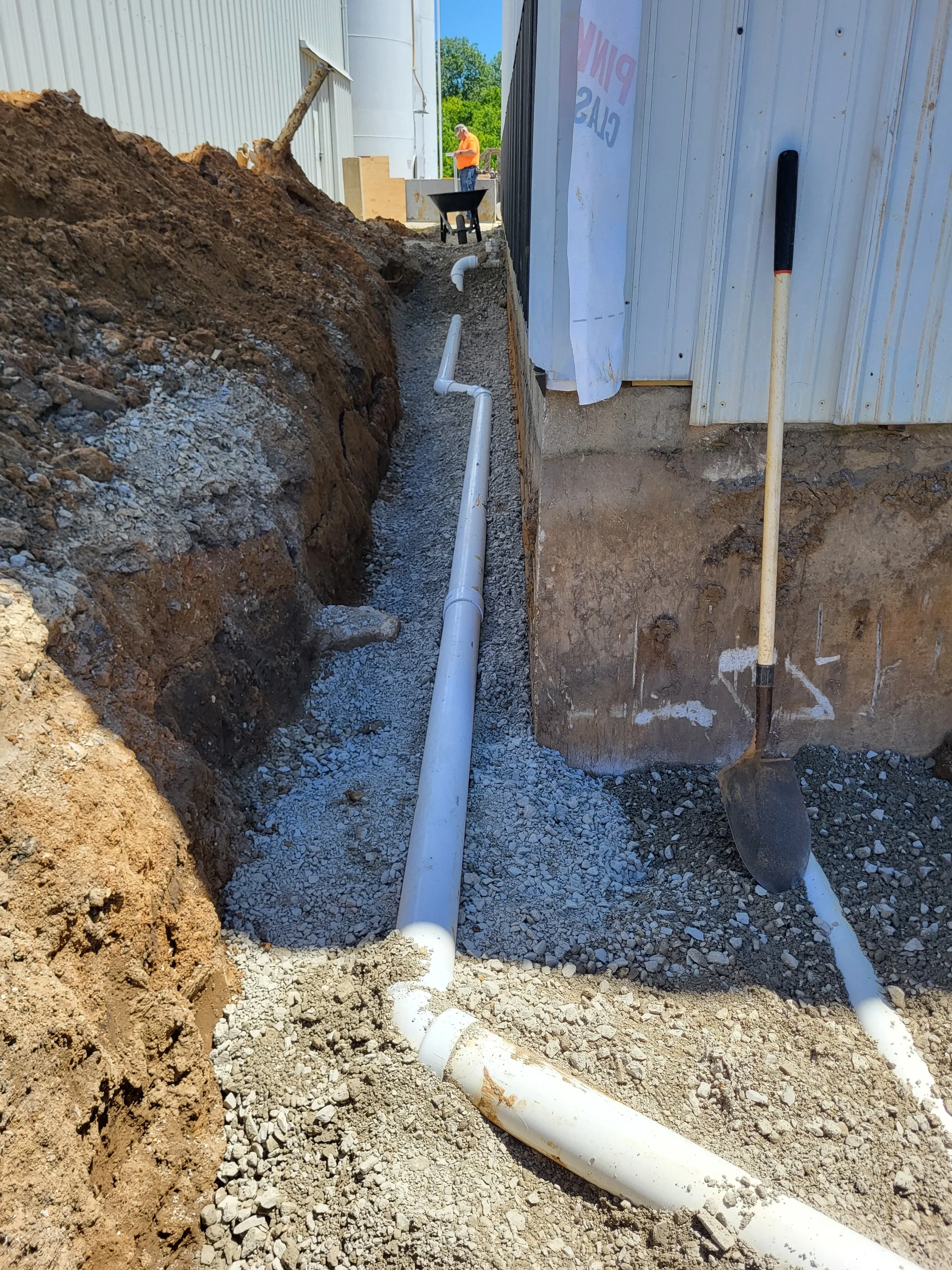 New white PVC drainage pipe installed in excavated trench with gravel base and compacted soil